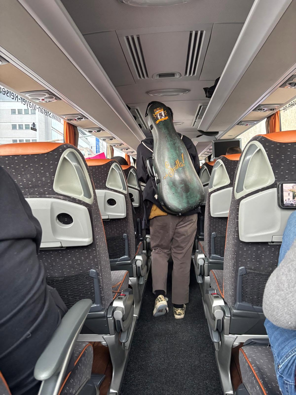 Musiker mit Cello-Case im Gang eines Reisebusses