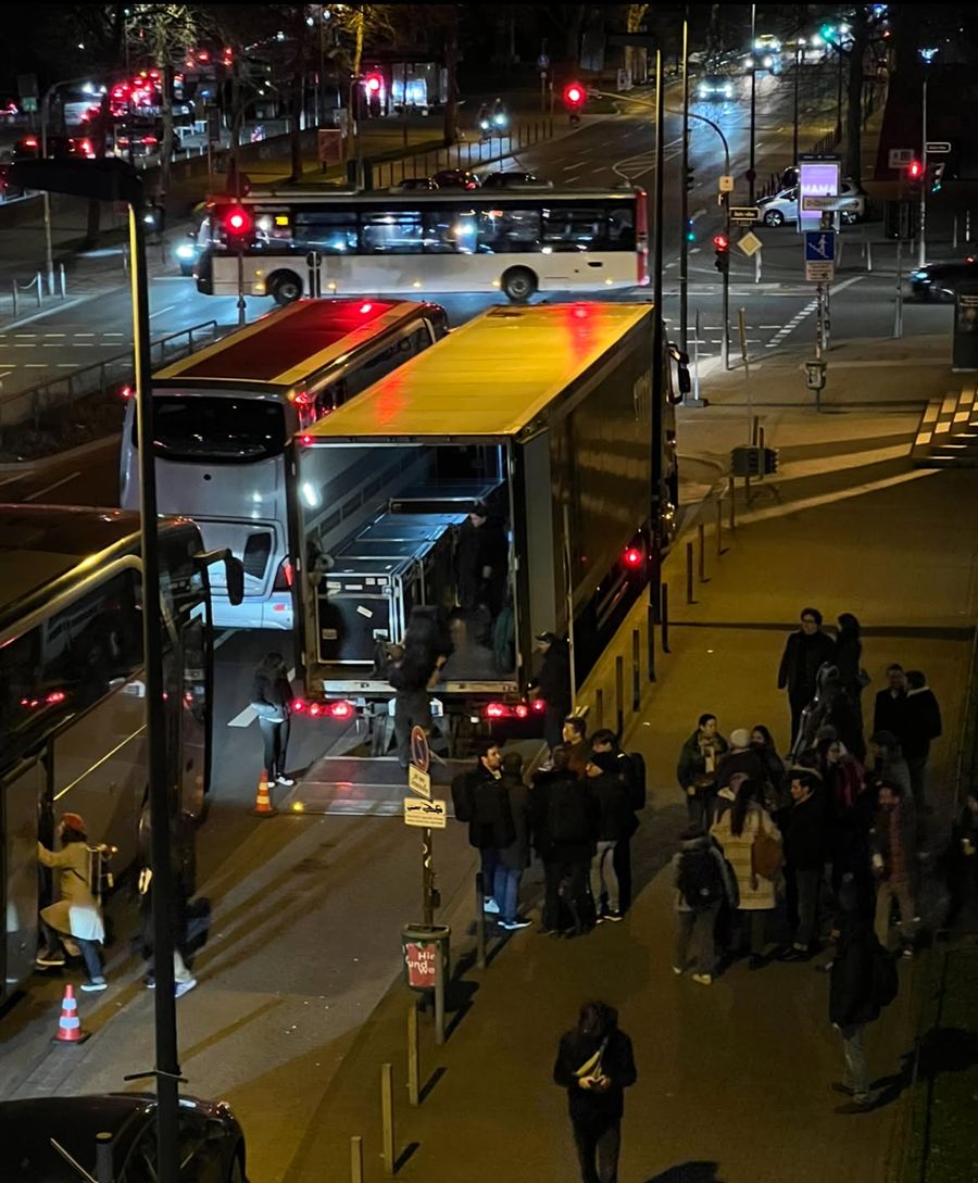Night load-out from above: coach, tour truck and musicians on the pavement